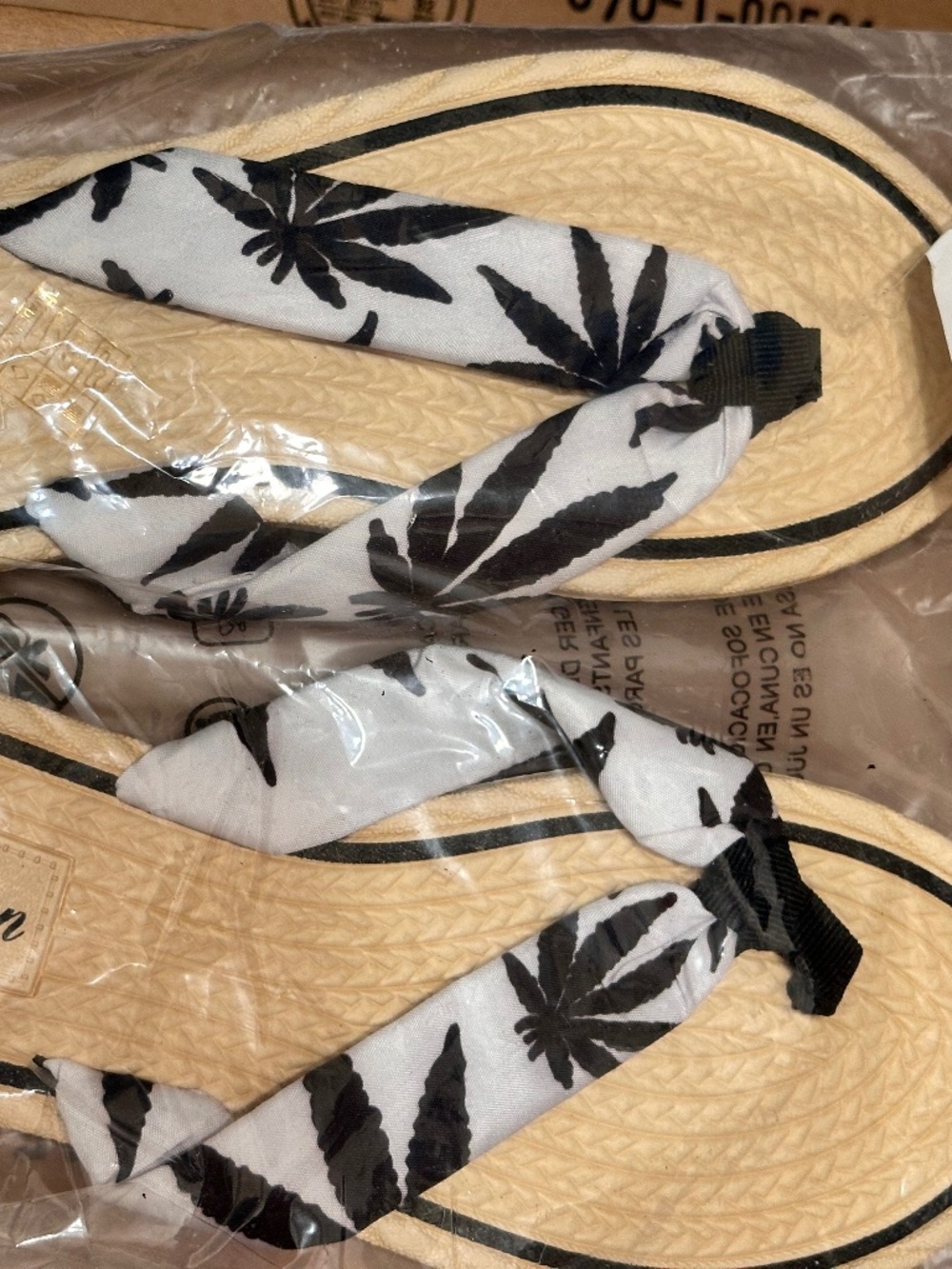 Fashion brand flip-flops feature a white fabric strap decorated with a black lea